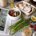 A selection of fresh vegetables and a cookbook in a kitchen setting, promoting healthy cooking.