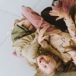 Mother and daughters laughing and bonding on the floor, capturing joyful family moments.